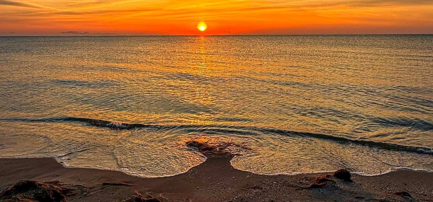 The waters edge at a beach with a golden orange and yellow sunset sky