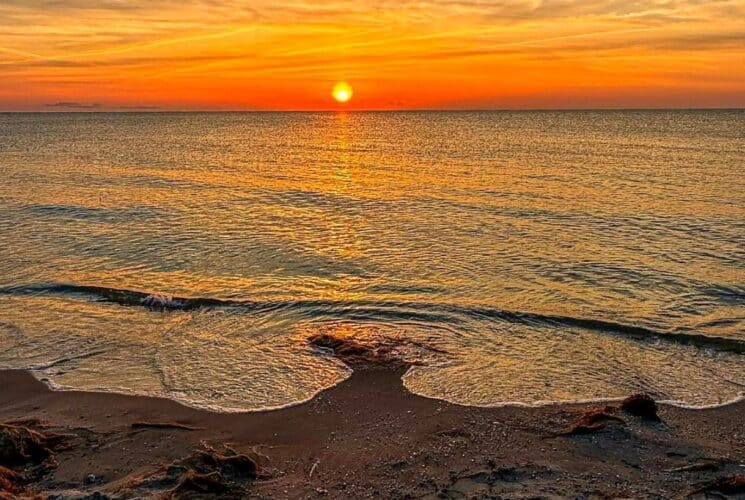 The waters edge at a beach with a golden orange and yellow sunset sky