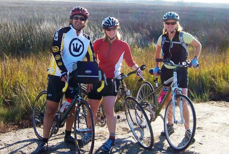 A group of three cyclists on a path outdoors in front of tall grass