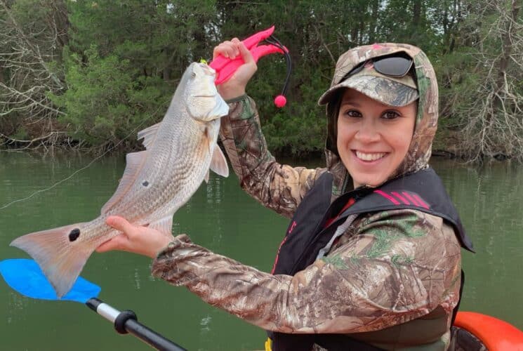 A woman in a camouflage jacket in a kayak holding up a large fish