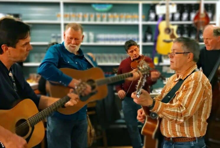 Five men standing in a store playing guitar, cello and violin