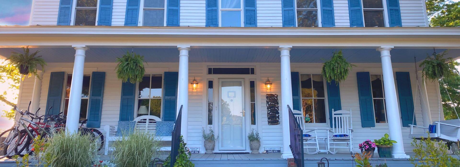 Exterior view of property painted white with blue shutters and front porch with white bench, white rocking chairs, and white bench swing