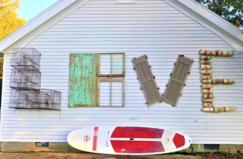 Exterior white wall decorated with old lobster cages, door, window, shutters, and buoys all arranged to spell the word LOVE