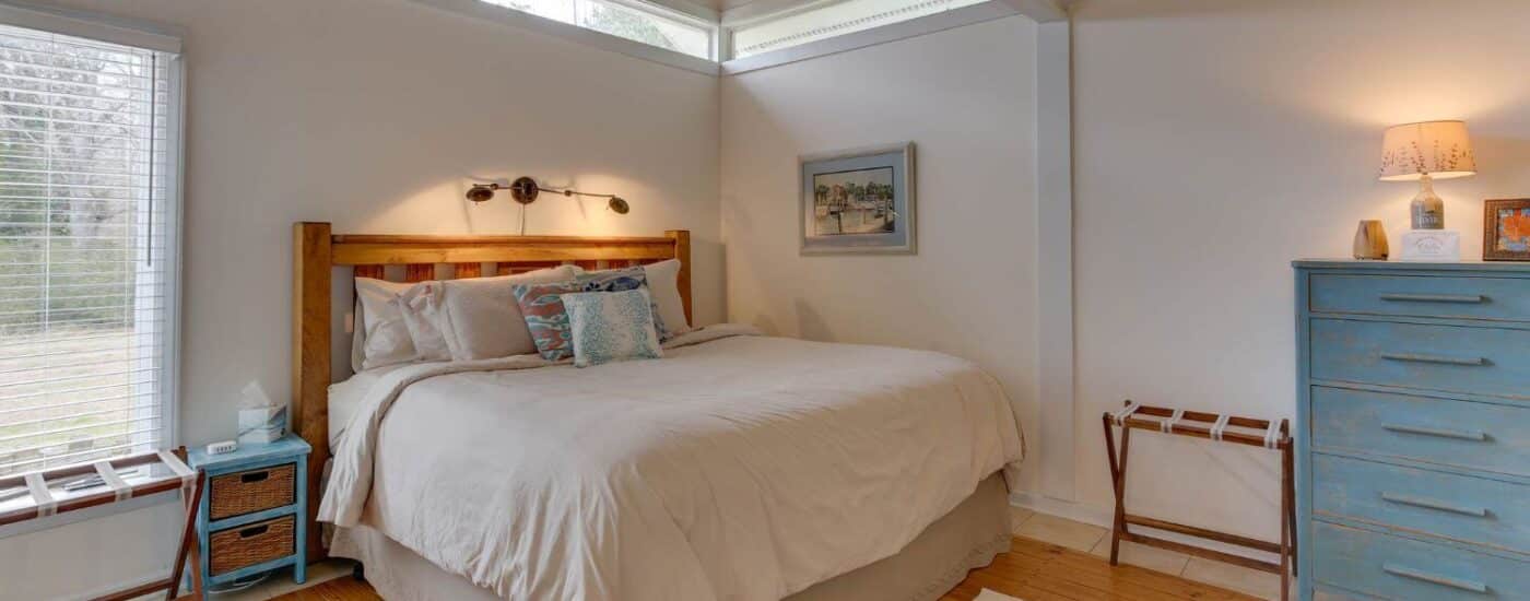 Bedroom with white walls, white trim, hardwood flooring, wooden headboard, and blue dresser