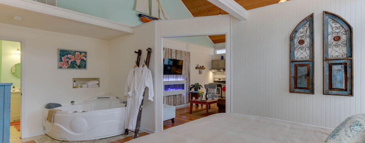 Bedroom with white walls, white trim, hardwood flooring, wooden headboard, and soaker tub