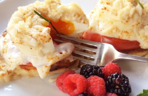 Close up view of Eggs Benedict and fresh berries on a white plate