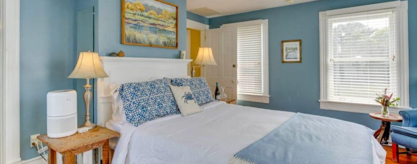 Bedroom with blue walls, white trim, light colored flooring, white headboard, and sitting area