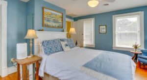 Bedroom with blue walls, white trim, light colored flooring, white headboard, and sitting area