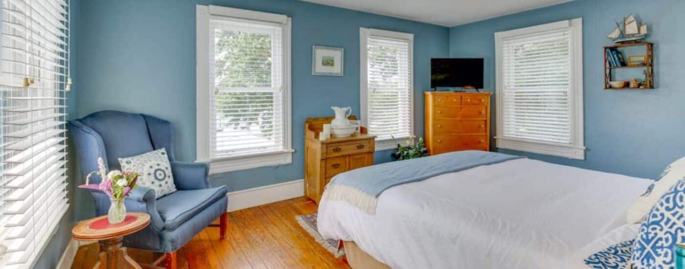 Bedroom with blue walls, white trim, light colored flooring, white headboard, sitting area, and wooden dresser