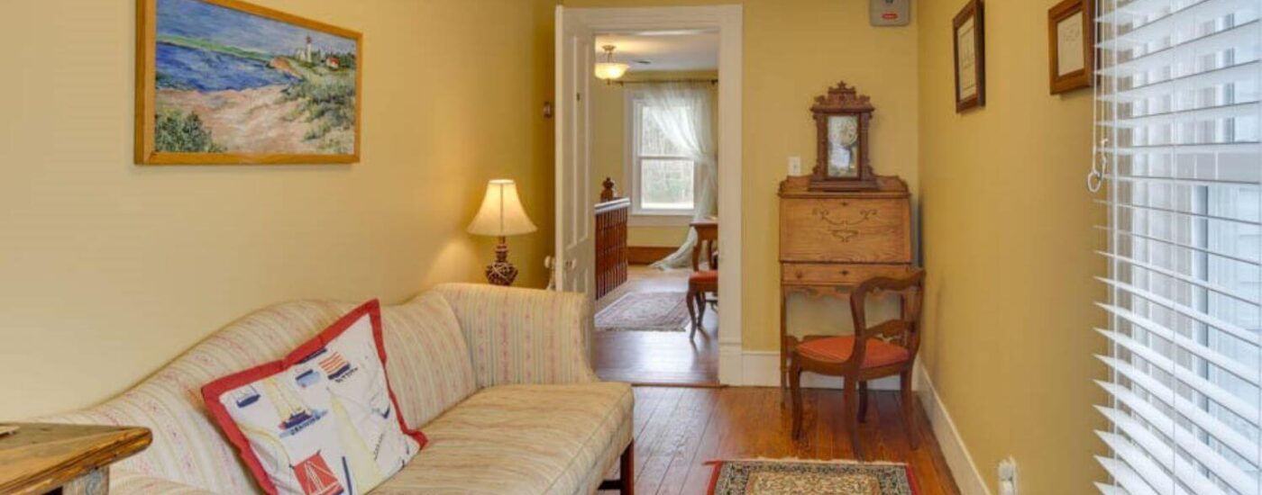 Adjoining room to bedroom with yellow walls, white trim, hardwood flooring, upholstered couch, and antique wooden desk with chair