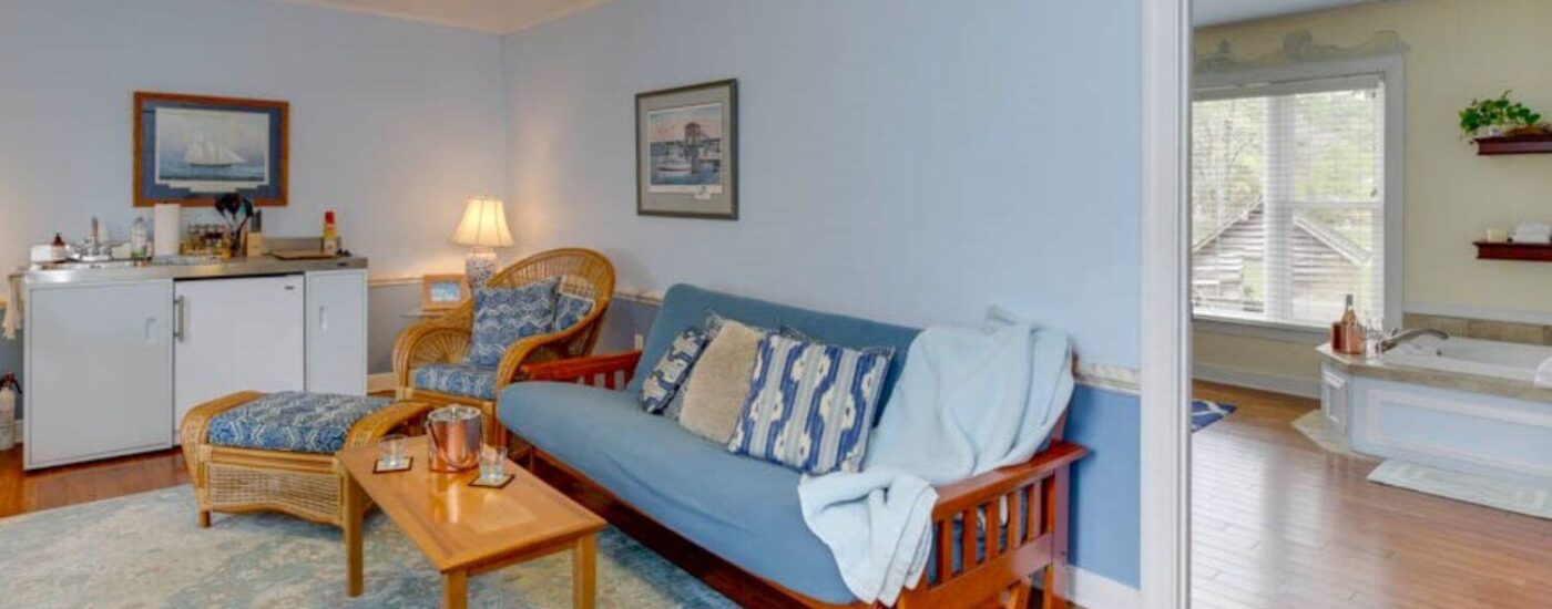 Adjoining room to bedroom with blue walls, white trim, hardwood flooring, futon, light brown wicker chair and ottoman, and coffee table