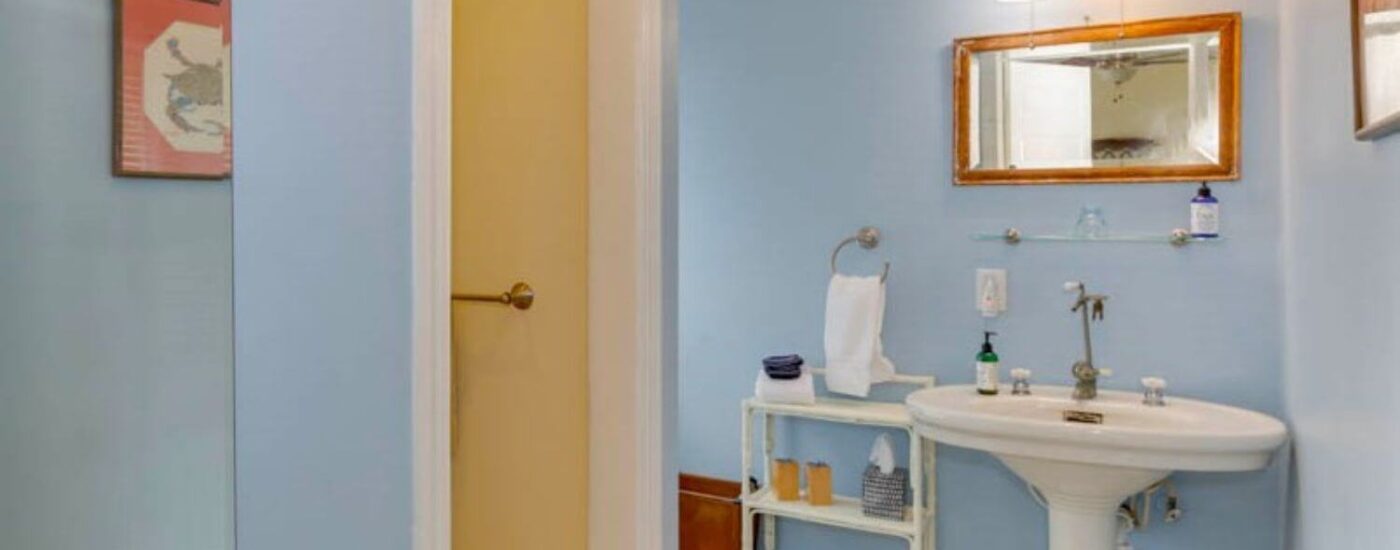 Bathroom with blue walls, tiled floor, white pedestal sink, and framed rectangular mirror