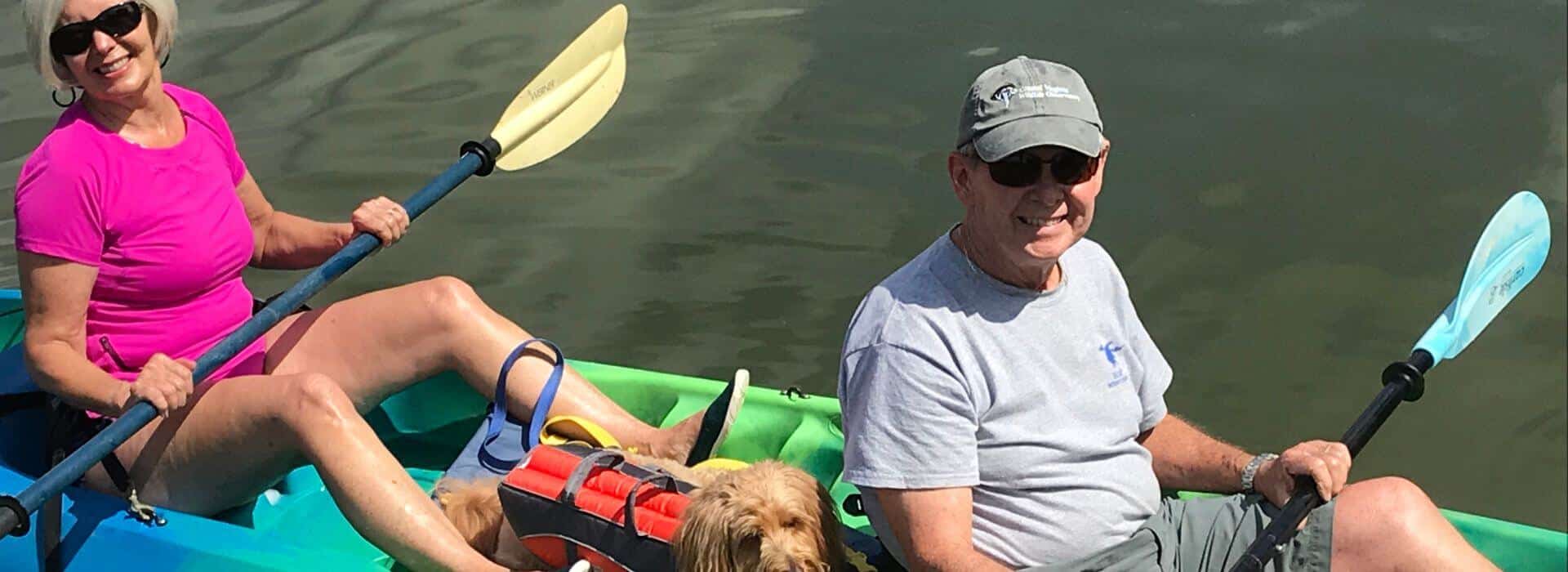 Woman, man, and dog on blue and green kayak