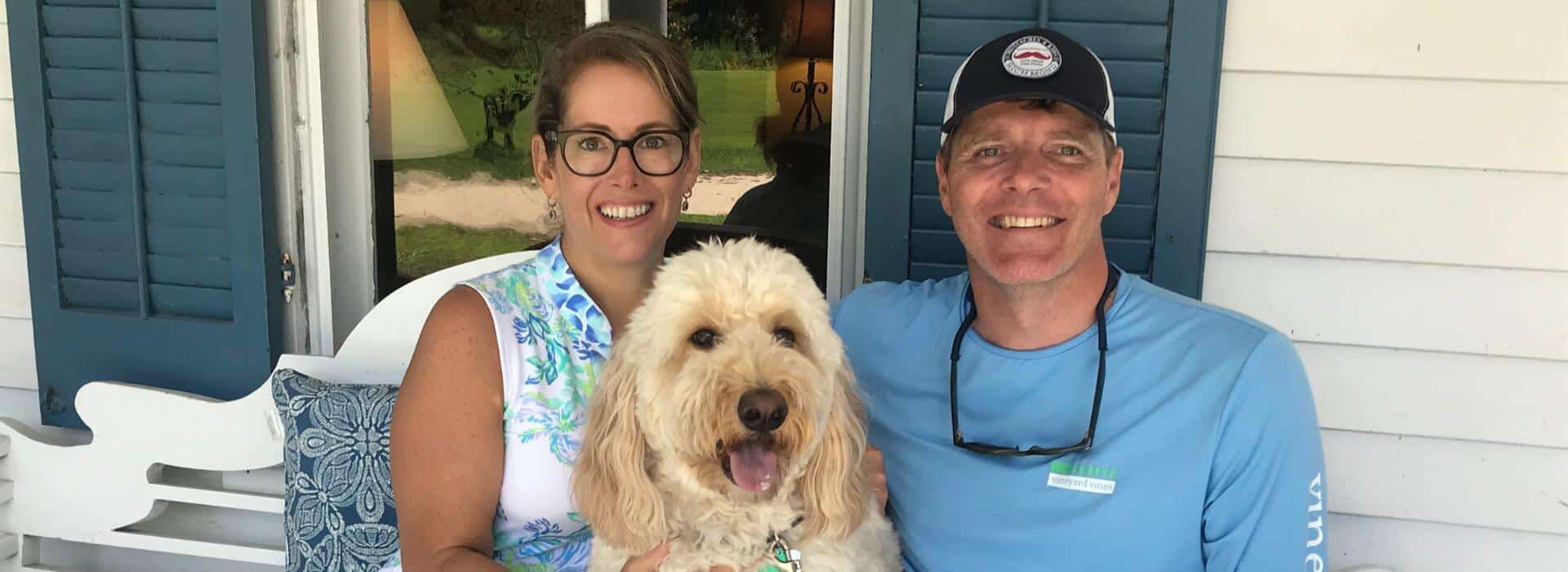 Woman, dog, and man sitting on white bench smiling for the camera