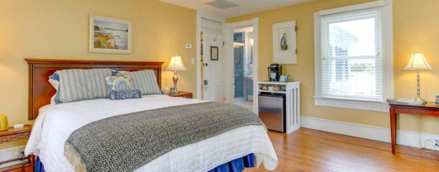 Bedroom with yellow walls, white trim, hardwood flooring, dark brown headboard, and stainless steel mini fridge