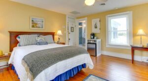 Bedroom with yellow walls, white trim, hardwood flooring, dark brown headboard, and stainless steel mini fridge