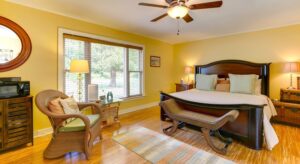 Bedroom with yellow walls, white trim, hardwood flooring, dark wooden bed, and light brown wicker chair with lime green cushion