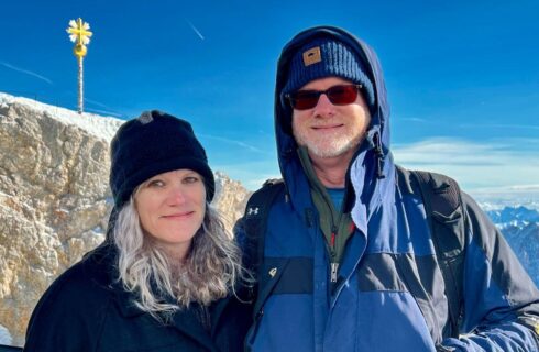 Woman and man wearing winter clothing with arms around each other standing on the top of a mountain