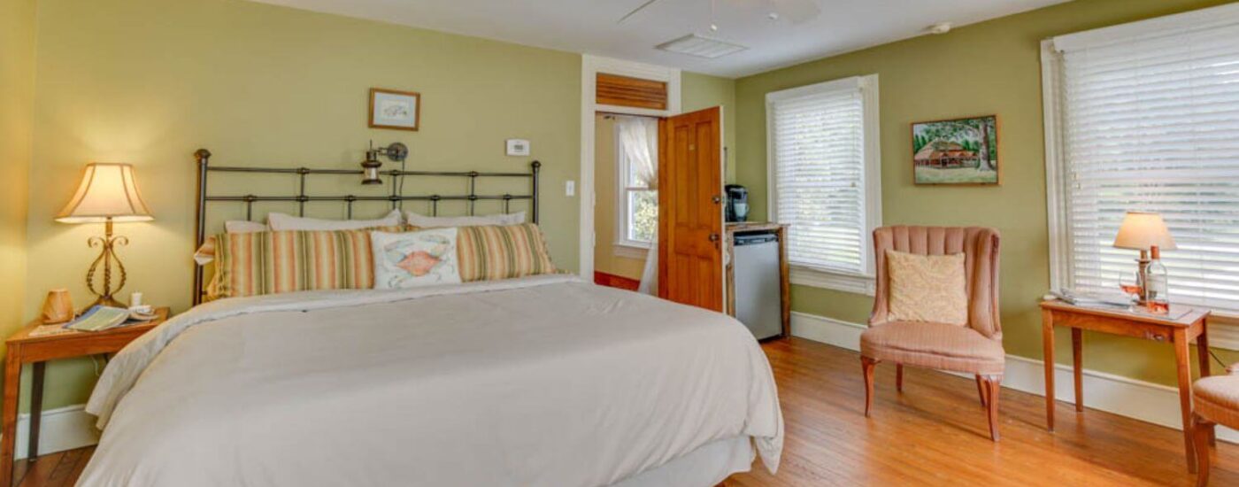 Bedroom with light green walls, white trim, hardwood flooring, iron headboard, and sitting area