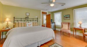 Bedroom with light green walls, white trim, hardwood flooring, iron headboard, and sitting area