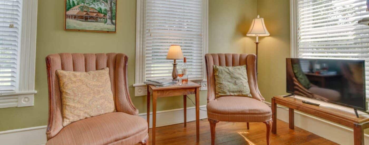 Bedroom's sitting area with light green walls, white trim, hardwood flooring, and flat-screen TV on a table