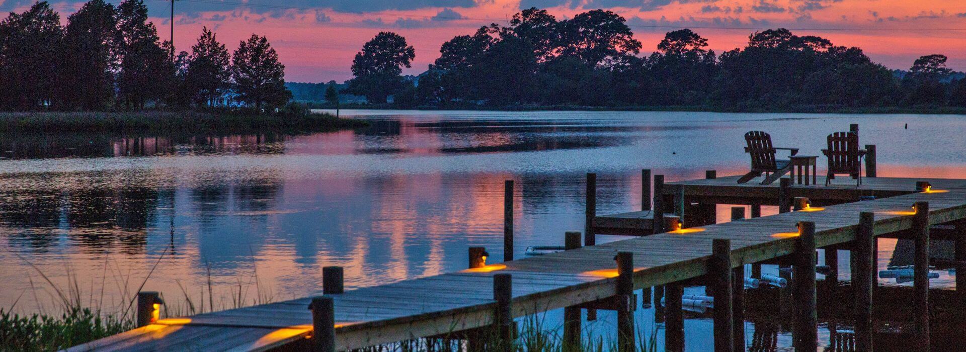 Dock illuminated with lights with calm water in the background at dusk