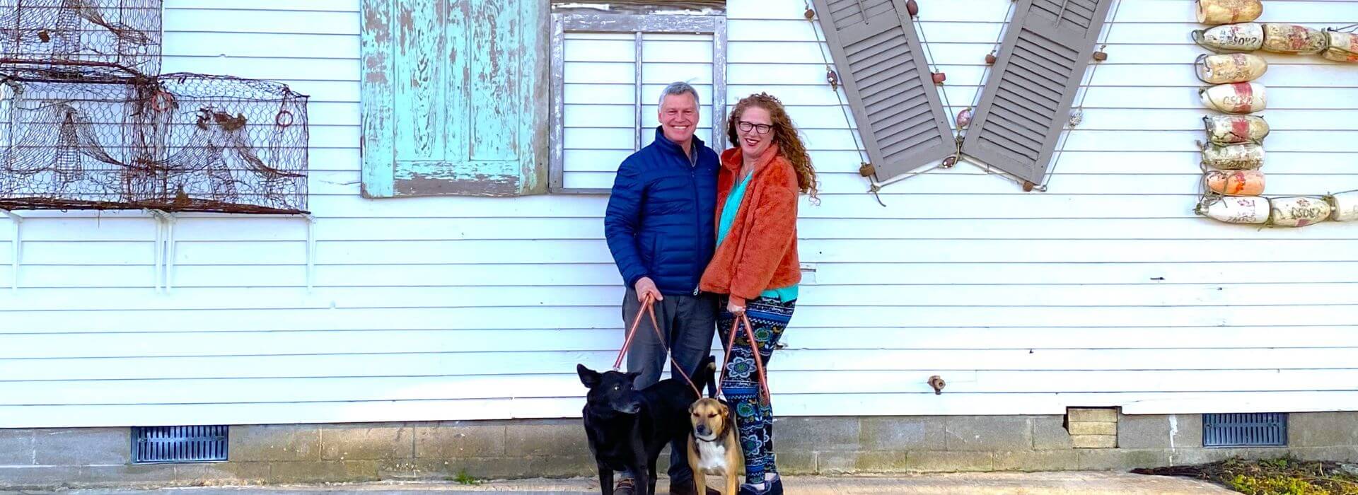 Man and woman wearing jackets standing together holding leashes of two dogs that are standing with them