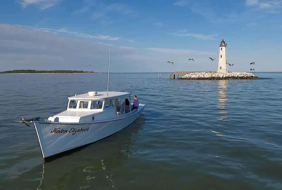 Small white boat on the water with a white lighthouse in the background