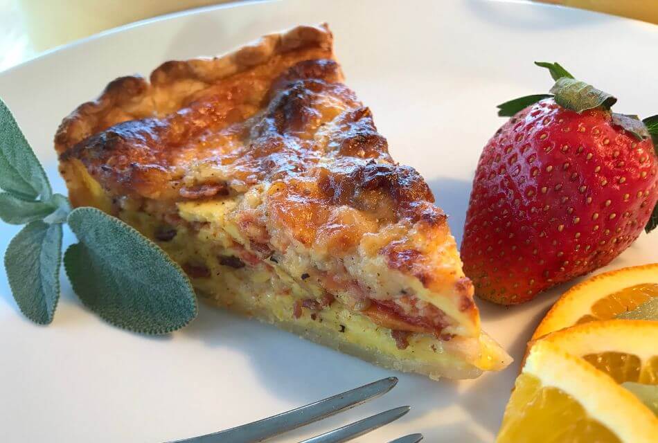 Close up view of breakfast quiche, strawberry, and orange slices on a white plate