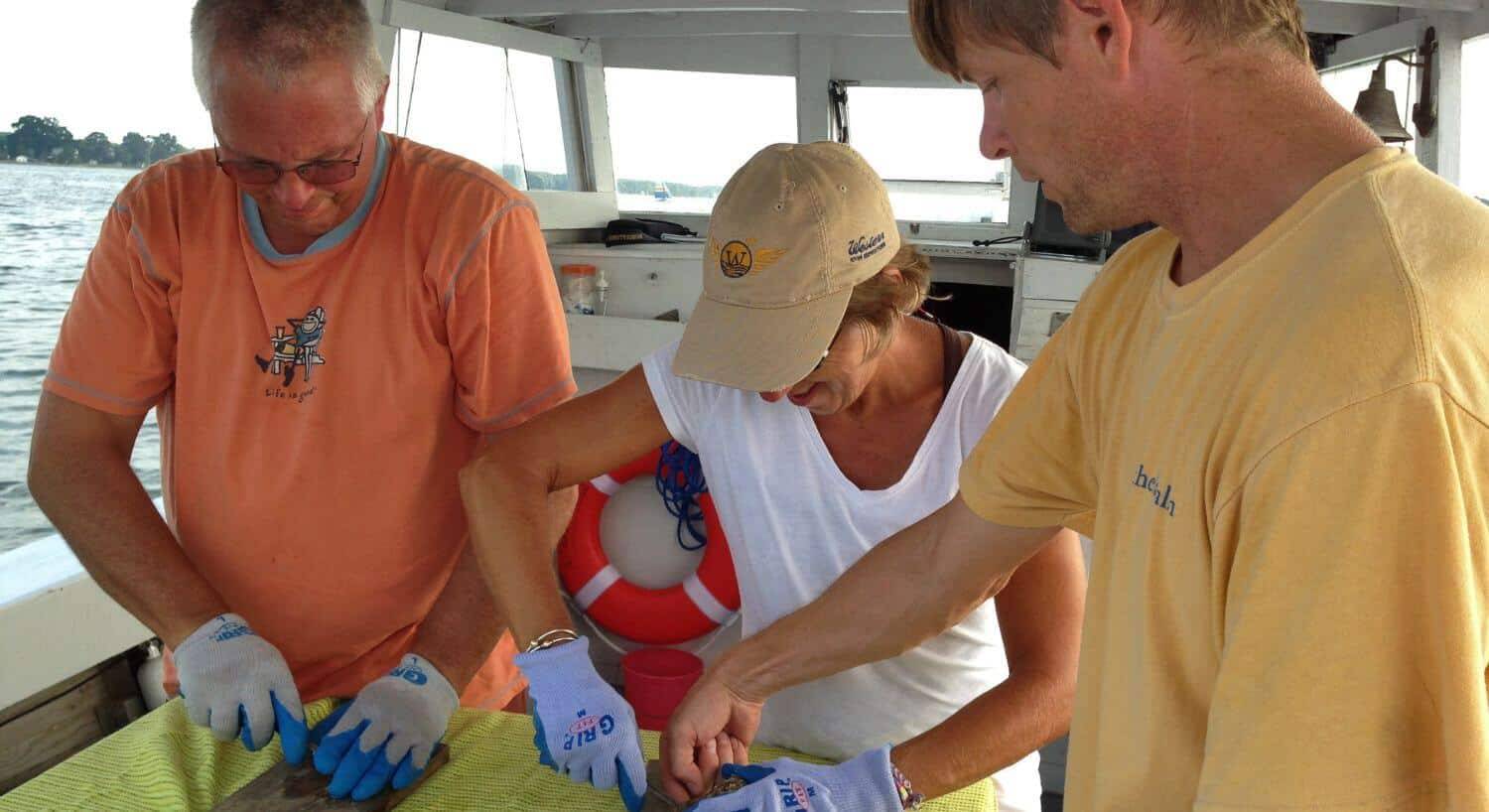 Two men and a woman shucking oysters on a small boat on the water