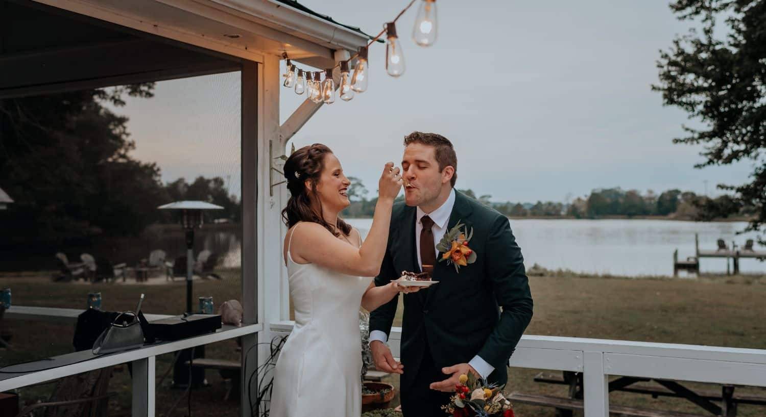 Bride serving groom cake on a patio with calm water in the background