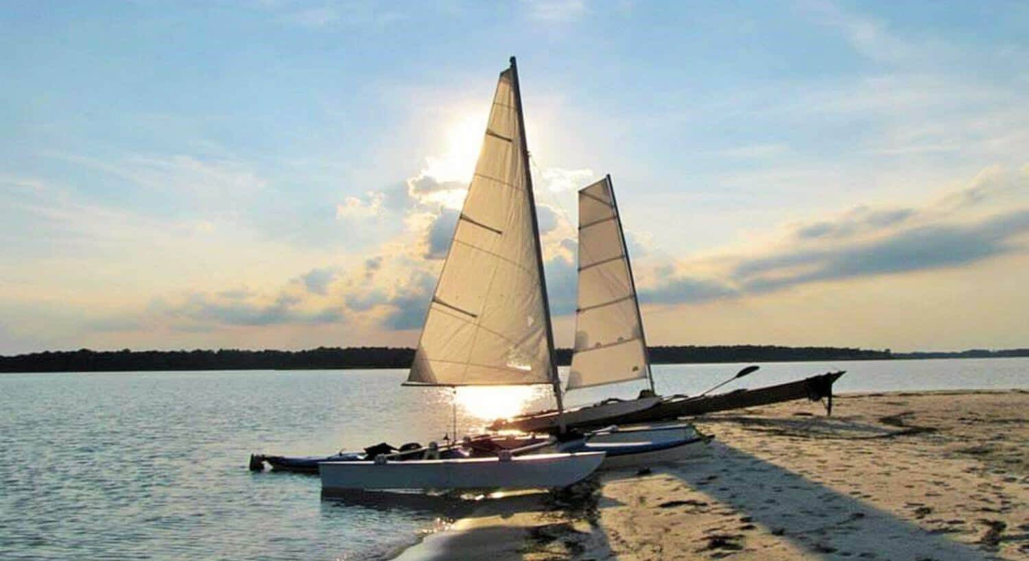 Two small catamarans anchored on a sandy beach next to the water