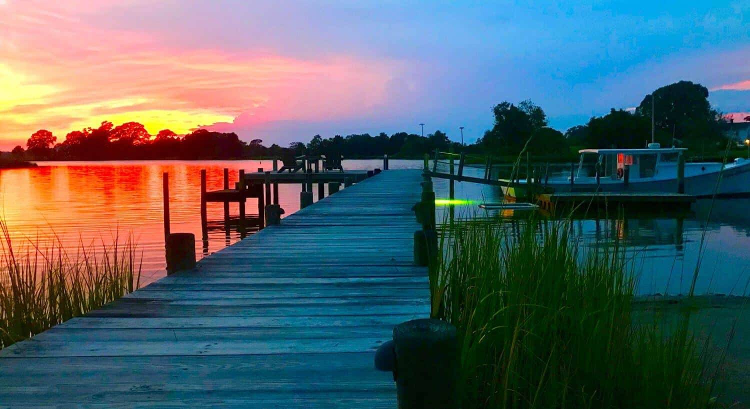 Small white boat docked at pier with calm water in the background at dusk