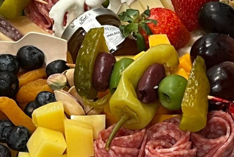 Close up view of charcuterie board with fruit, cheese, meat, veggies, pickles, olives, and white chocolate covered pretzels