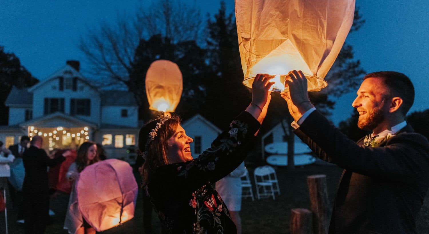 Multiple people getting ready to release lighted paper lanterns into the night sky