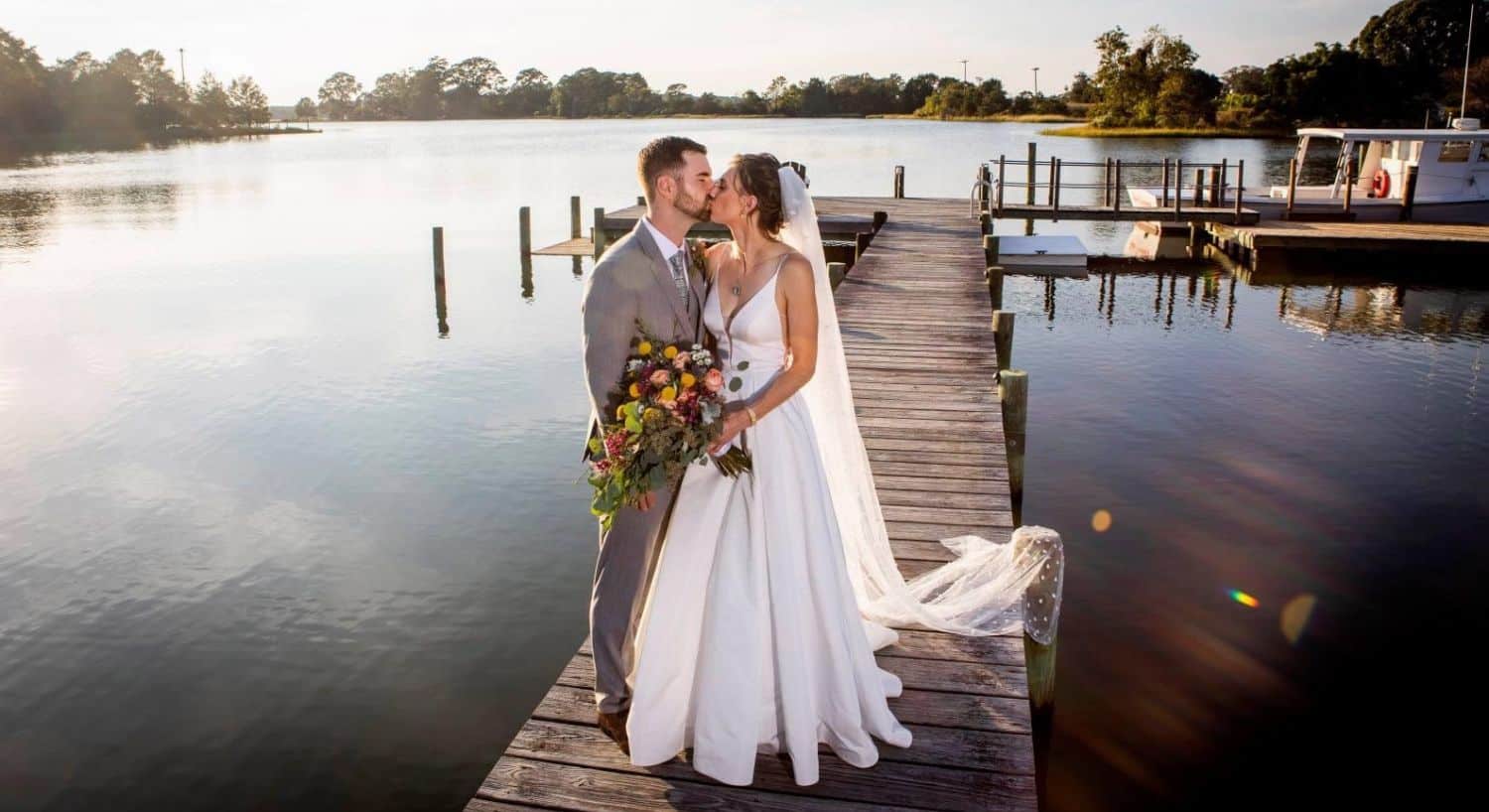 Bride and groom standing and kissing on a pier with calm water in the background