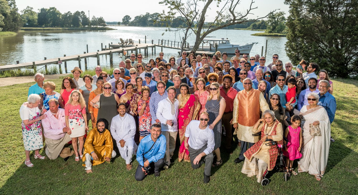 Large group of people on green grass posing for a picture with dock and water in the background