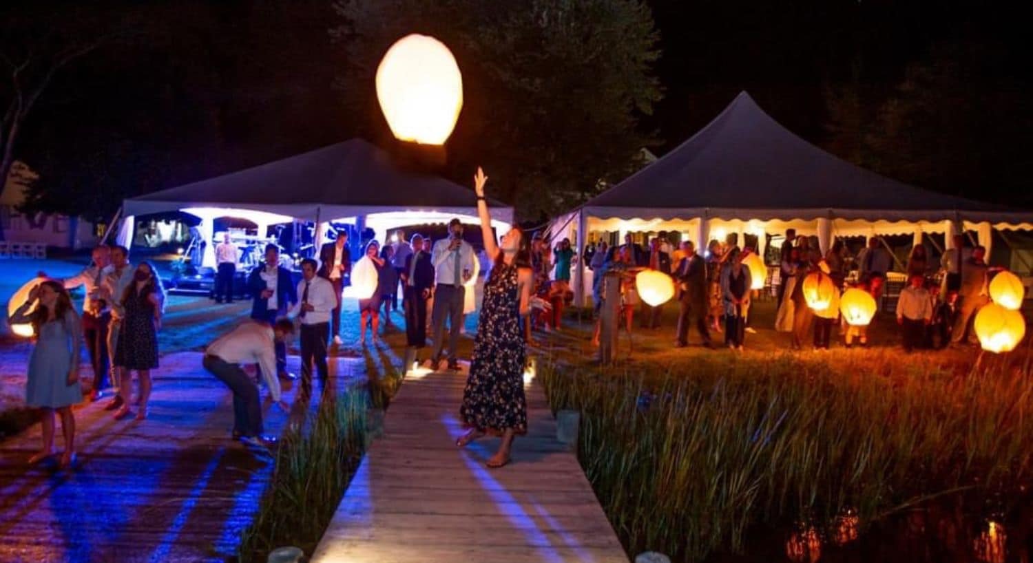 Multiple people getting ready to release lighted paper lanterns into the night sky