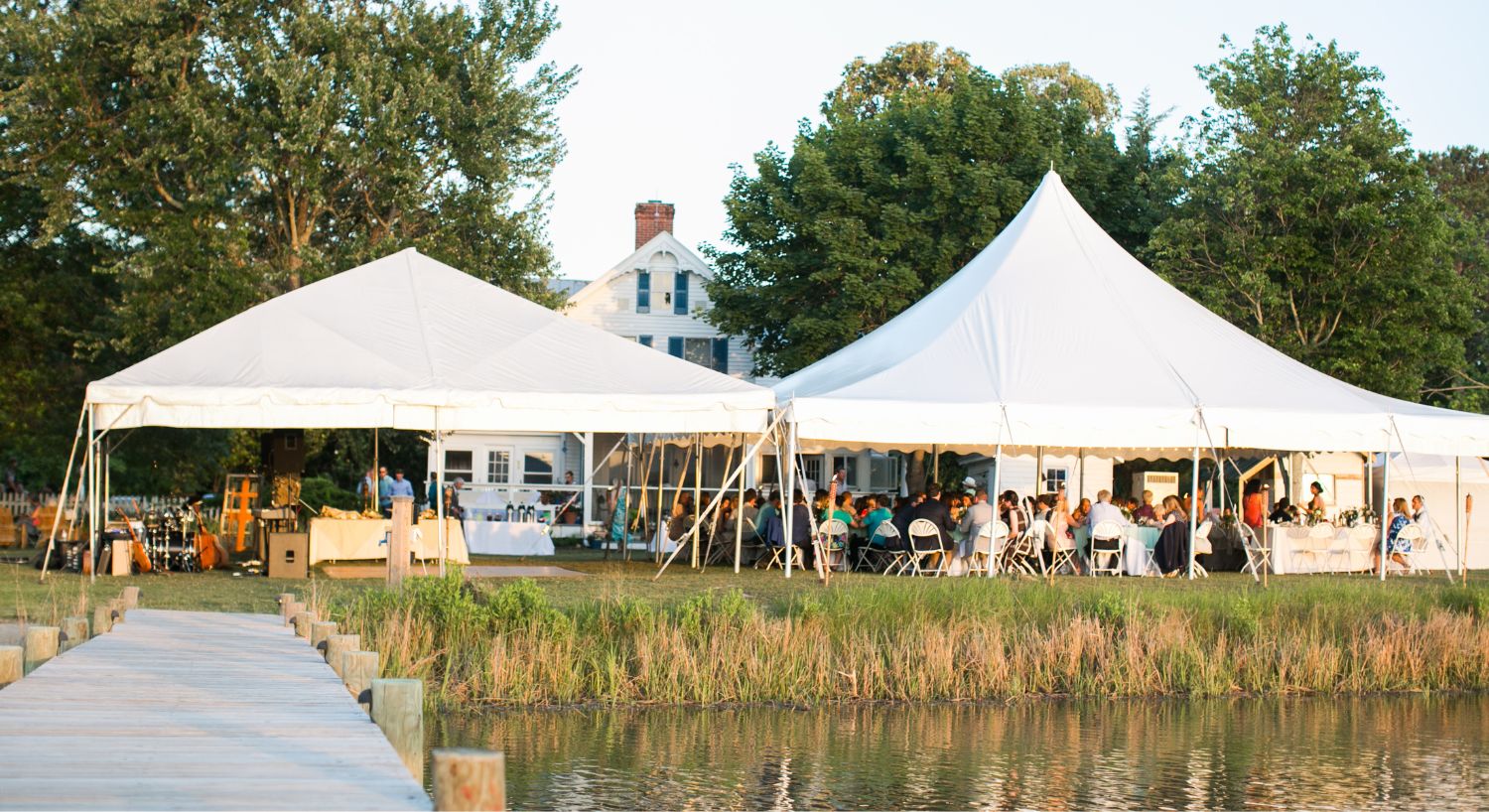 Two large white tents set up on green grass for a wedding near the water