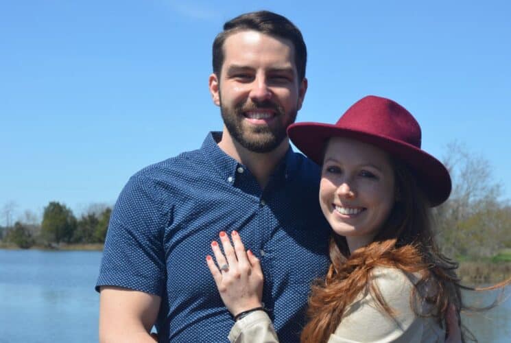 Man and woman holding each other smiling at the camera with calm water in the background