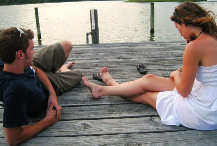 Man and woman leisurely sitting on a dock with calm water in the background